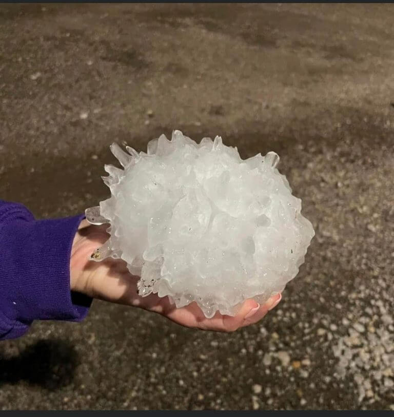 A young boy displays a massive hailstone gripped firmly in his hand.