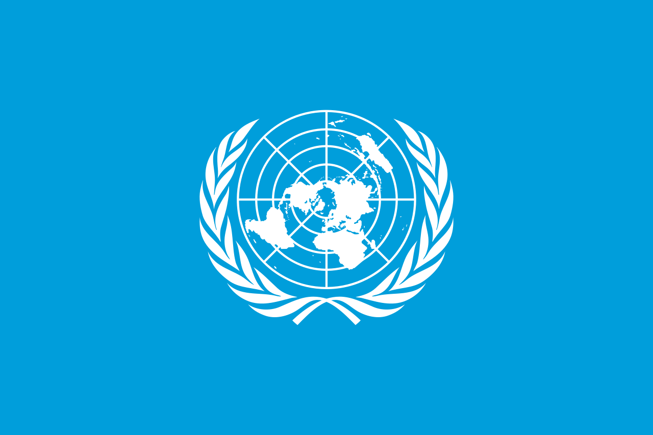 The United Nations flag flying proudly against a clear blue sky, featuring a light blue emblem of a world map surrounded by olive branches, symbolizing peace and unity.