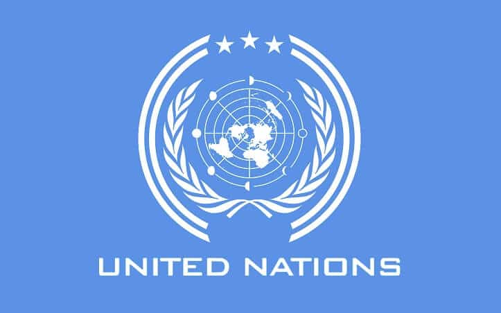 The United Nations flag flying proudly against a clear blue sky, featuring a light blue emblem of a world map surrounded by olive branches, symbolizing peace and unity.